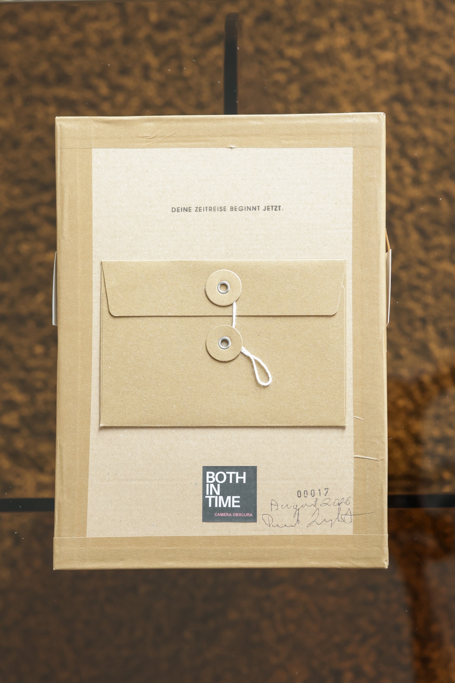 Die Rückseite einer Both In Time Kamera aus Kraftpapier: ein Umschlag mit Kordelverschluss und der Aufkleber mit Seriennummer.
